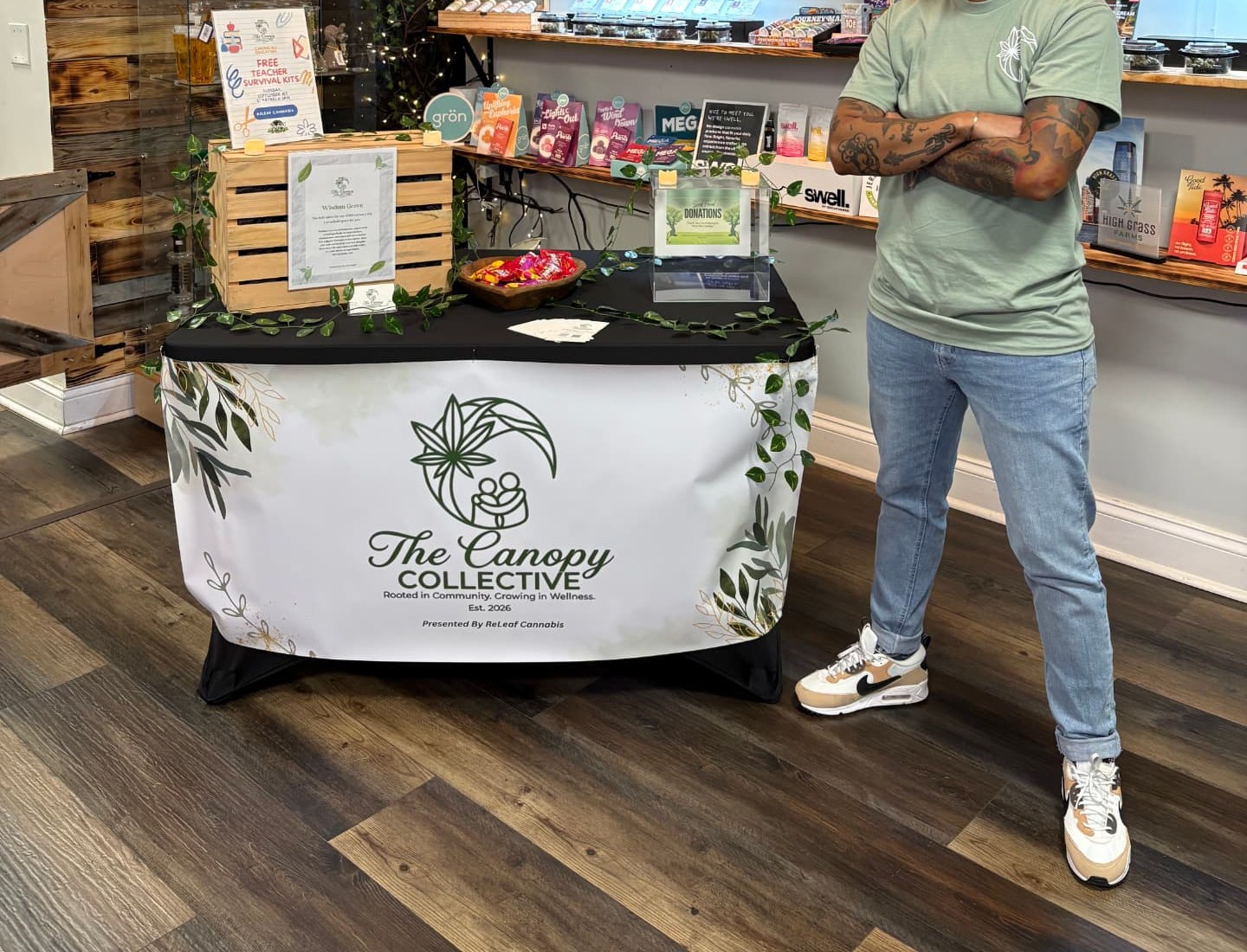 A community member standing beside The Canopy Collective table at a gathering.